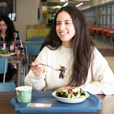students1 student siting at a table eating a salad and smiling